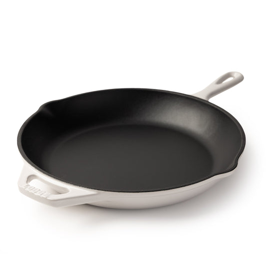 An enameled cast iron skillet with a black interior and a white exterior, featuring a single loop handle on the right and a side handle on the left, photographed on a clean white background.