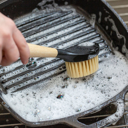 Someone scrubbing their cast iron grill pan with brush and soapy water.