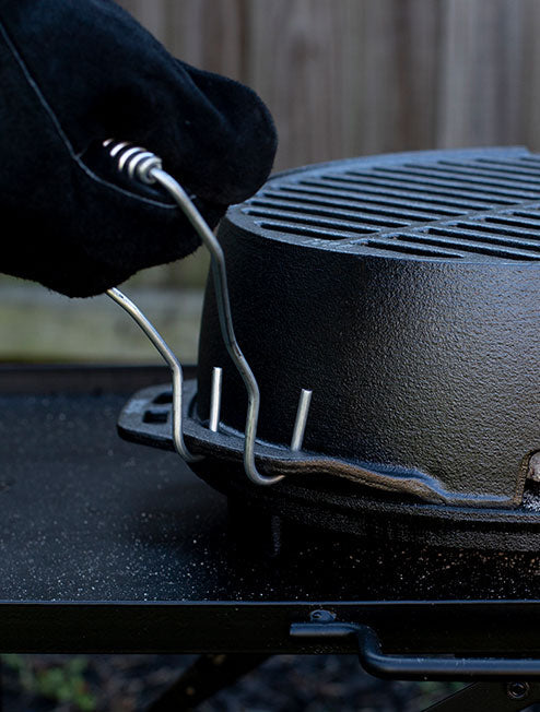 A close-up image of a black grill with a person's hand adjusting a steel handle that is attached to the grill.