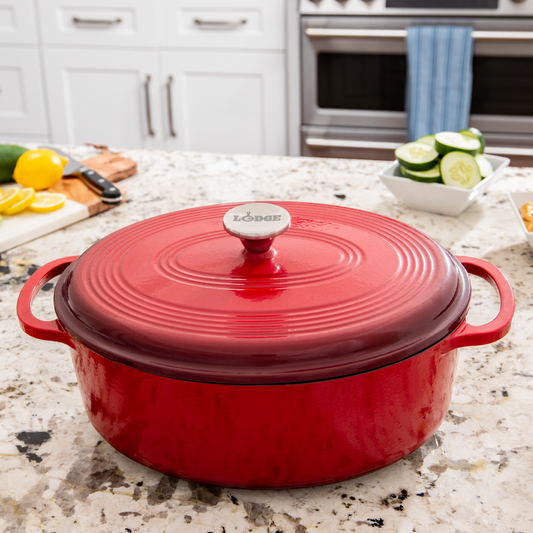 A red enameled cast iron Dutch oven with a lid and metal handles, displayed in a kitchen setting.