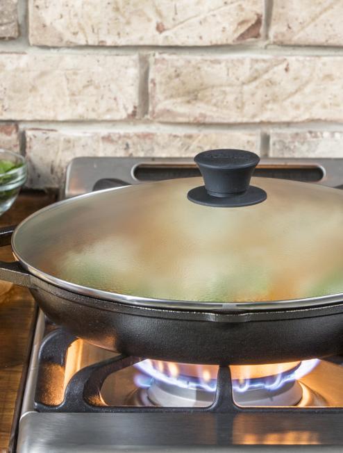 Vegetables being steamed on stovetop with cast iron skillet and lid.