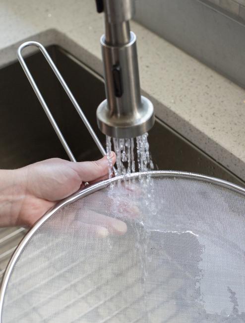 Someone rinsing splatter screen under running water in sink.