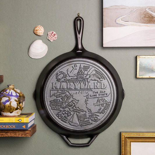 Decorative cast iron skillet with 'Maryland' design on a wall with books and seashells.