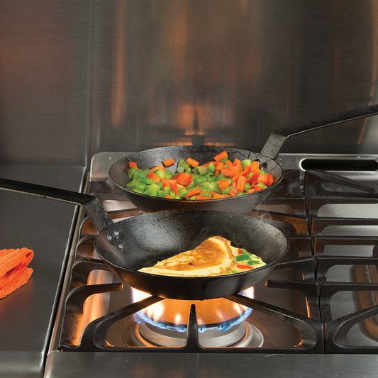 Two skillet cooking peppers and an omelet on stove.