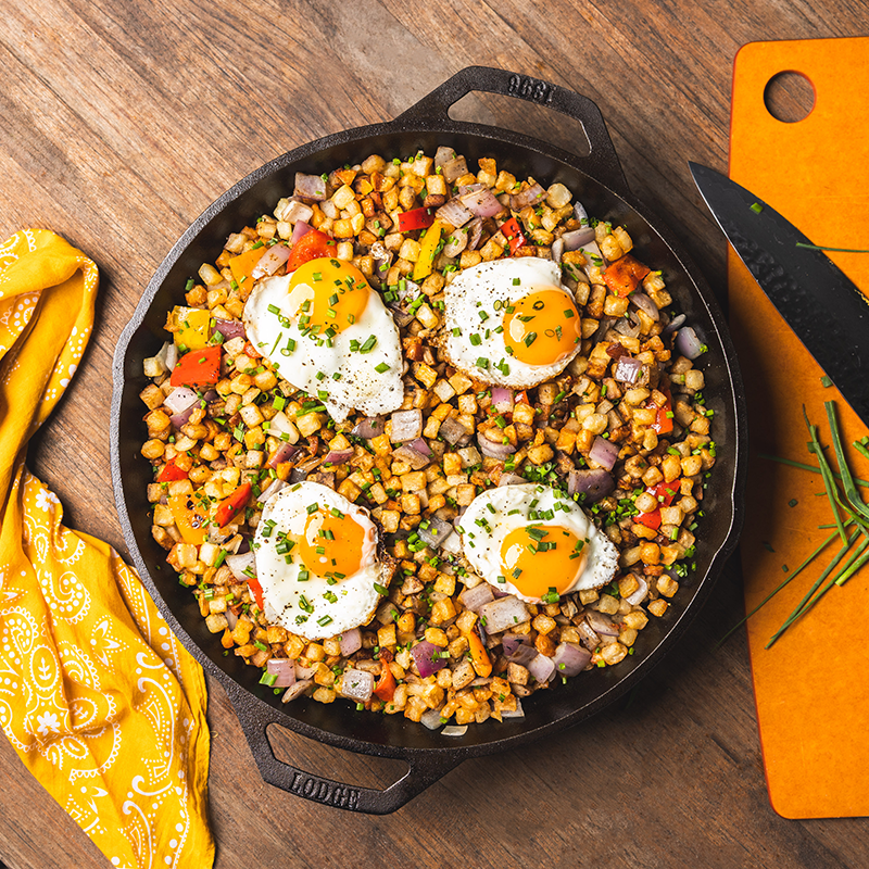 Skillet with breakfast hash and eggs on a wooden table