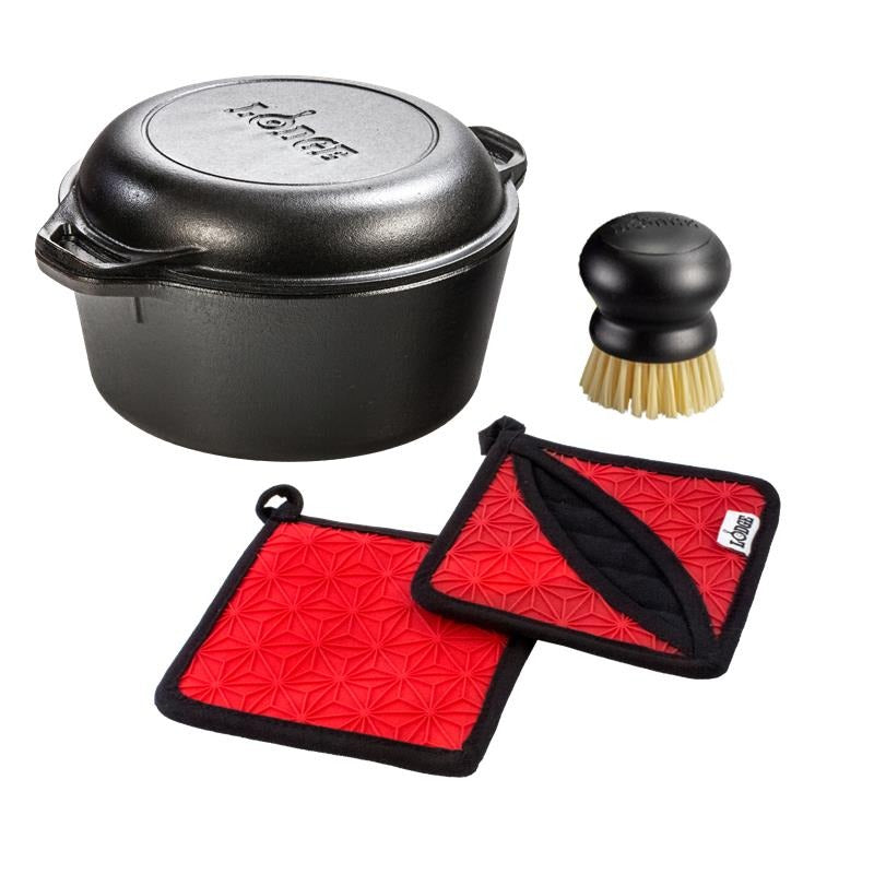 Black cast iron dutch oven with lid, brush, and red pot holders on a white background