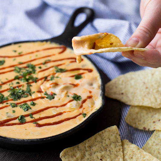 Someone using a tortilla chip to eat our skillet queso recipe.