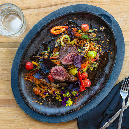 Delicate dish of beef with vegetables on a cast iron serving griddle with a blue underliner, served on a kitchen table.