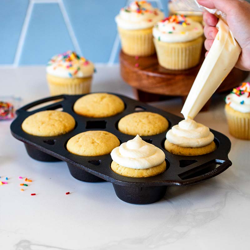 Someone icing cupcakes after baking them in pan.