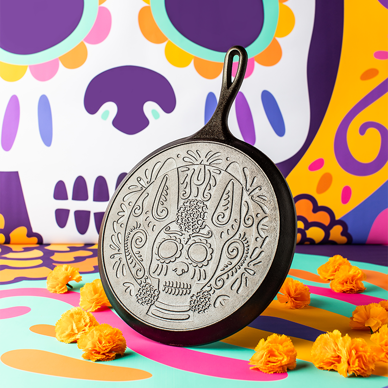 Decorative cast iron skillet with skull design on a colorful abstract background
