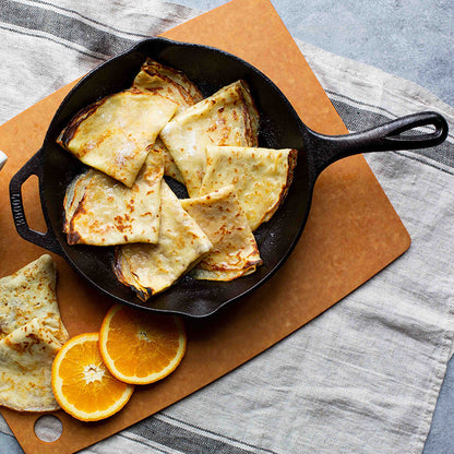 Freshly made crepes, served in skillet near oranges.