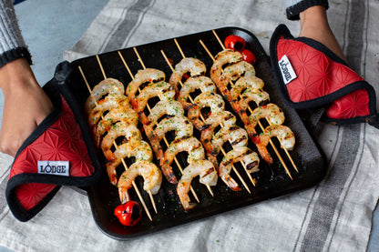Someone using handle holders to carry our grill pan after cooking shrimp skewers.