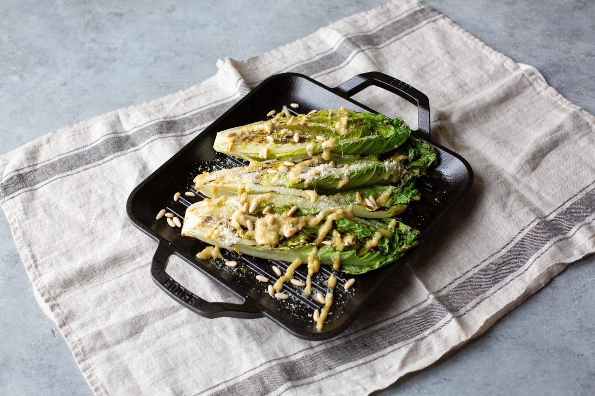 Grilled romaine presented on table topped with dressing and nuts.