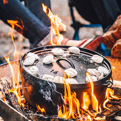Dutch oven cooking on fire with coals on top.