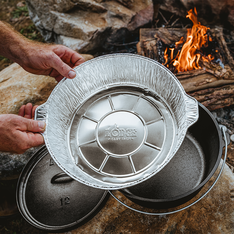 Someone getting ready to use liner in camp dutch oven over a firepit.