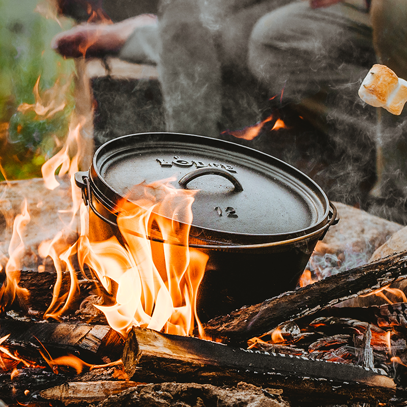 Dutch oven cooking on fire with coals on top.