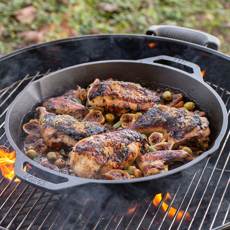 Chicken and olives being cooked in pan on a charcoal grill.
