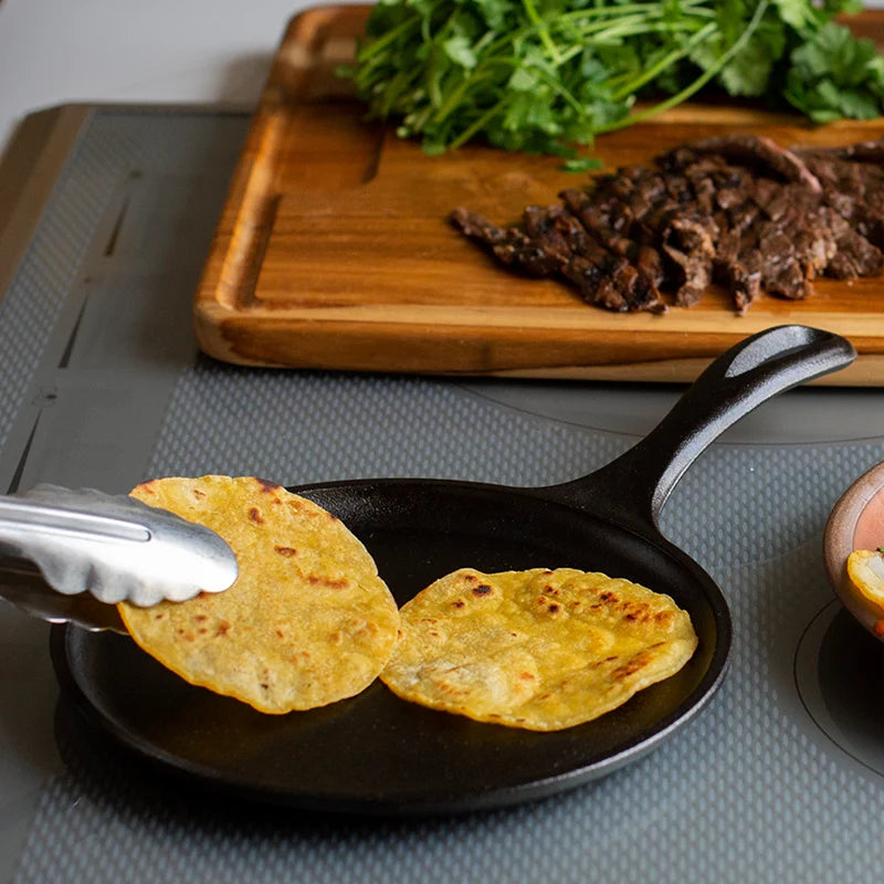 Someone flipping cooked tortillas on griddle to use for their steak tacos.