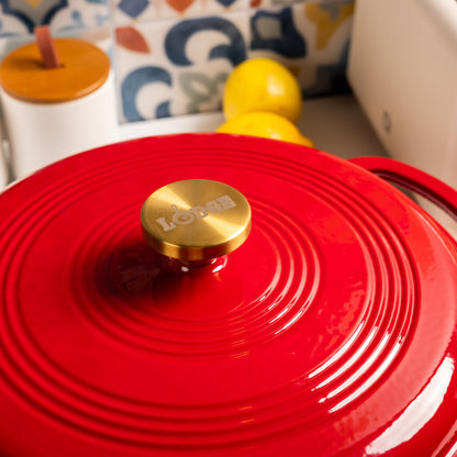 Red lid with a gold knob featuring the brand 'Lodge' on a blurred kitchen background.