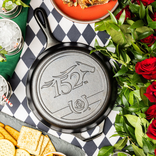 Seasoned Cast Iron Kentucky Derby Skillet for the 152nd year, placed on checkered table surrounded by food and roses.