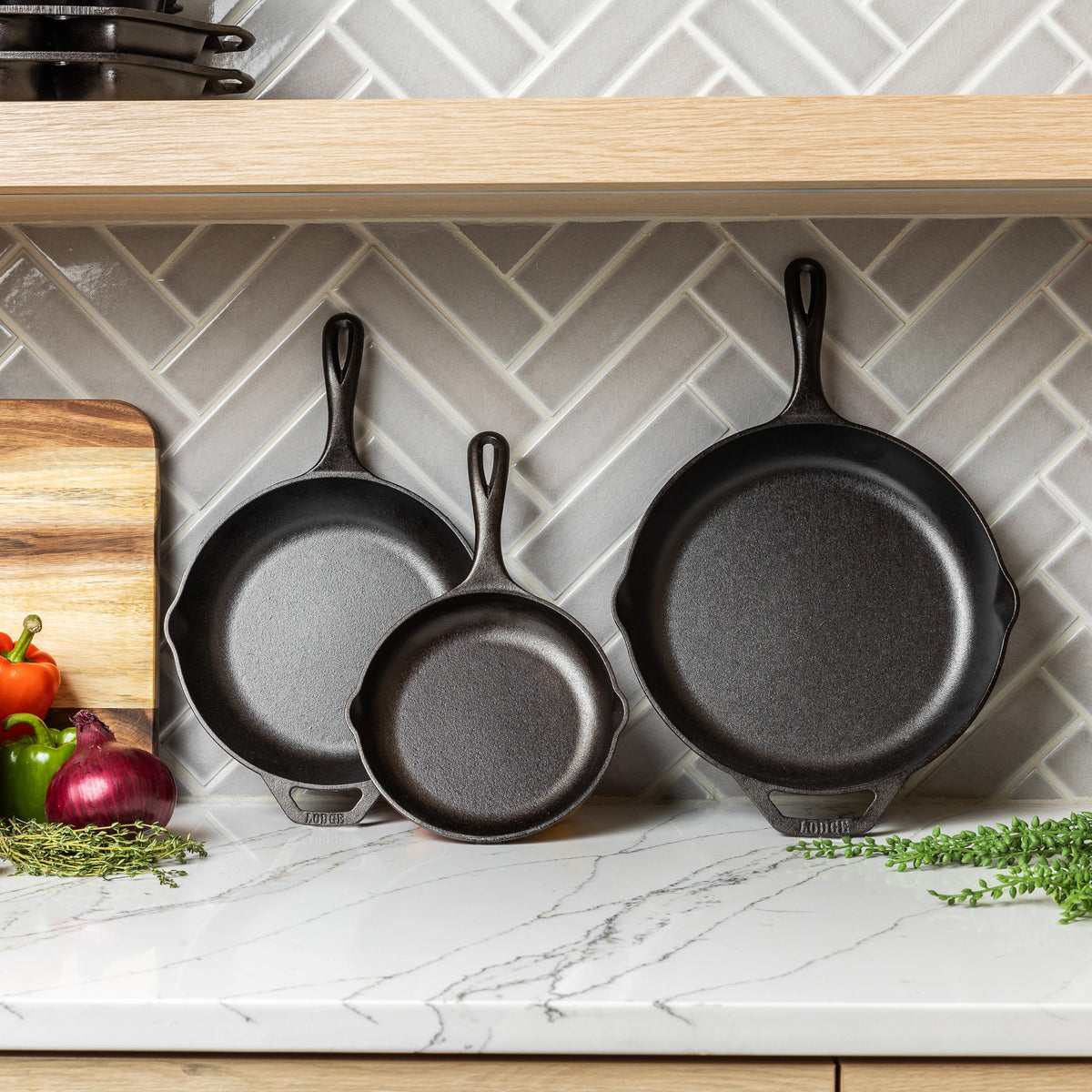 Set of cast iron skillets on a kitchen counter with vegetables and a cutting board.