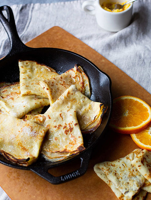 Freshly made crepes, served in skillet near oranges.