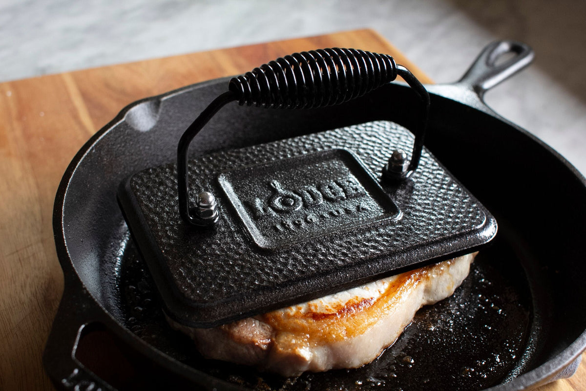 Grill press on top of steak cooking in skillet.