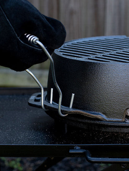 A close-up image of a black grill with a person's hand adjusting a steel handle that is attached to the grill.