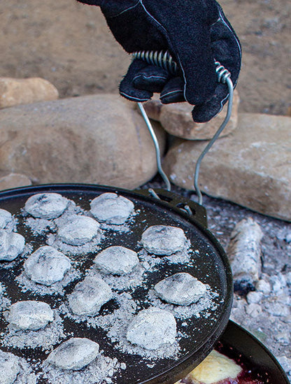 Someone using handles while lift lid filled with hot coals while cooking.