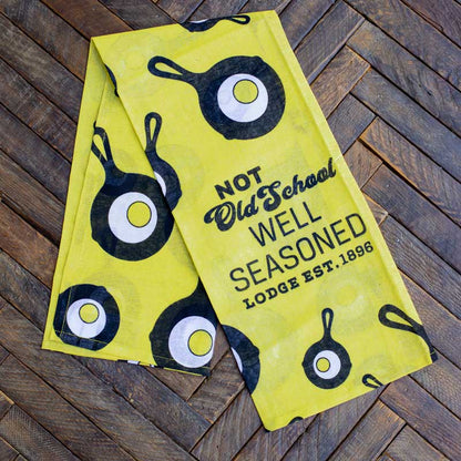 Towel placed on wooden surface, partially unfolded to show the Lodge skillet and egg logo scattered throughout.