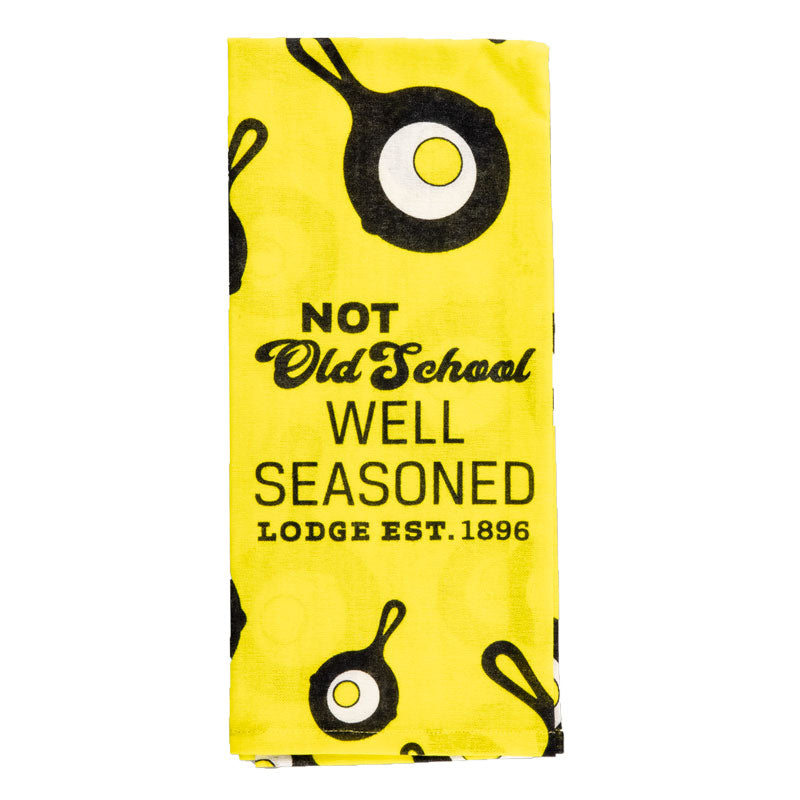 Yellow towel, with the Lodge skillet and egg logo through out and text saying "Not Old School Well Seasoned Lodge Est. 1896" in the middle of towel while folded.