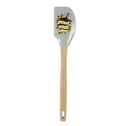 Spatula with wooden handle and decorative head, a skillet and pastry design and a ribbon with text "Bake it... bake it real good" in front on a gray background.