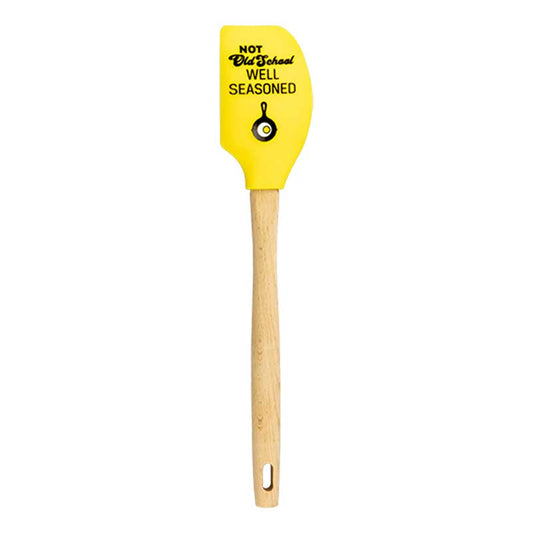 Yellow spatula with wooden handle and black text saying "Not Old School Well seasoned" above the Lodge skillet and egg logo.