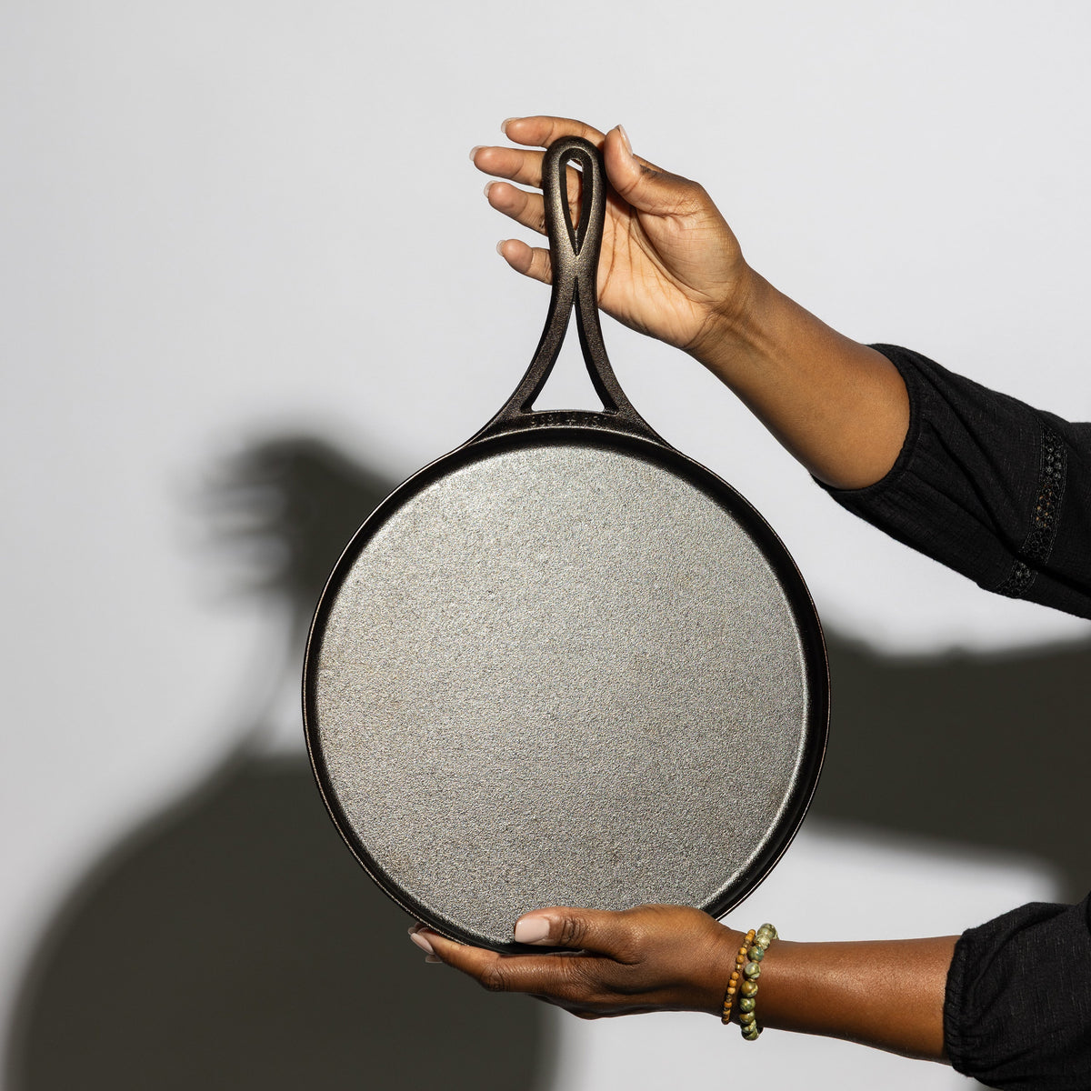 A person holding a round cast iron griddle.