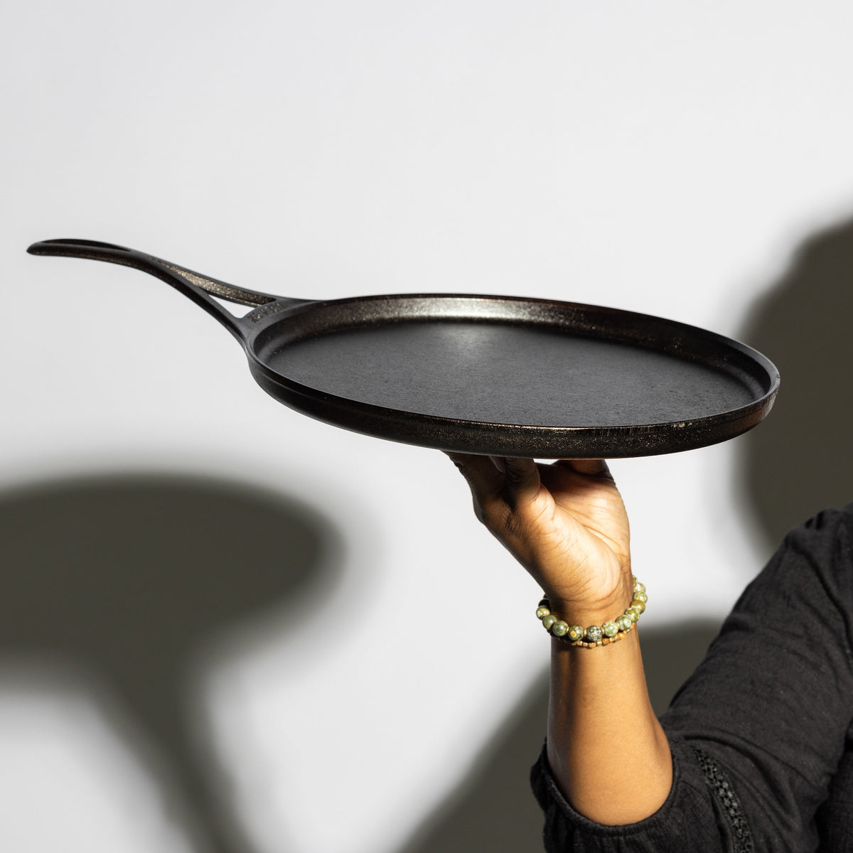 A hand holding a dark cast iron skillet against a light gray background with soft shadows.