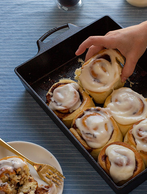 Someone taking a freshly baked cinnamon rolls from casserole pan.