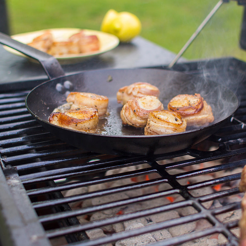 Scallops being cooking on skillet over charcoal grill.