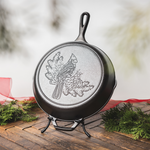 Cast iron skillet with a cardinal engraving, displayed on a Lodge Skillet Display stand with a festive holiday background.