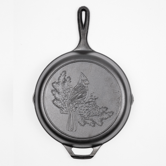 Cast iron skillet with a Cardinal engraved on the back who is perched on balsam fir branches.