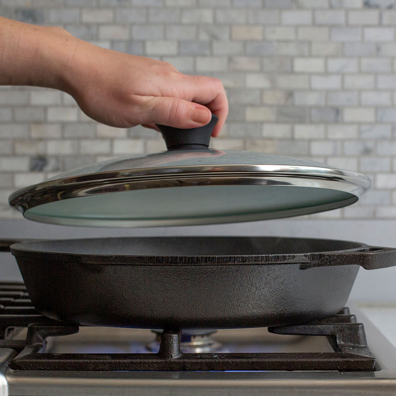 Someone placing lid on skillet while cooking on stove.