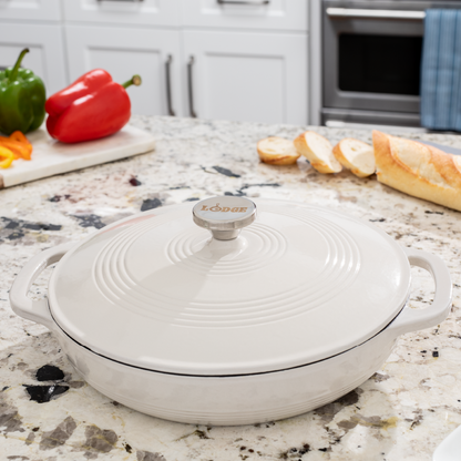 Braiser on kitchen counter in front of fresh peppers and sliced bread.