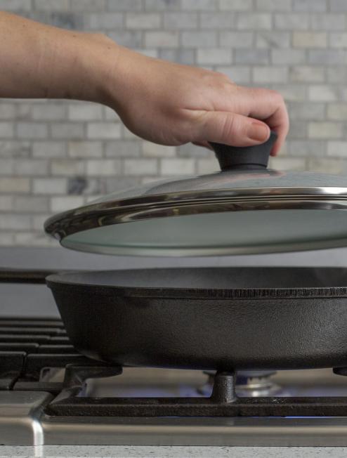 Someone placing lid on skillet while cooking on stove.