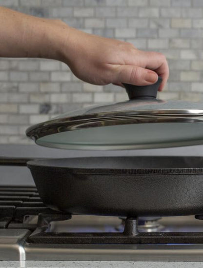 Someone placing lid on skillet while cooking on stove.