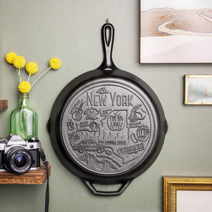 Decorative state cast iron skillet hung a wall with a camera and flowers below.