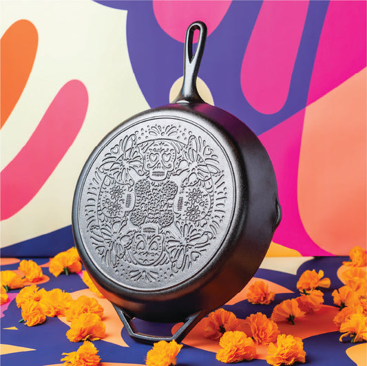 Decorative black cast iron skillet with floral patterns on a colorful abstract background with orange flowers.
