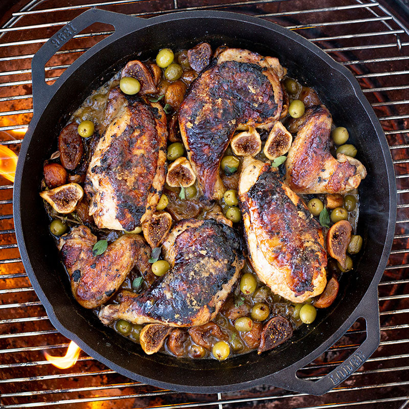 Chicken and olives being cooked in pan on a grill.