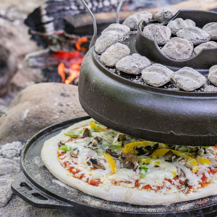 Someone lifting the lid with hook and carry handles revealing a pizza being baked on the griddle.