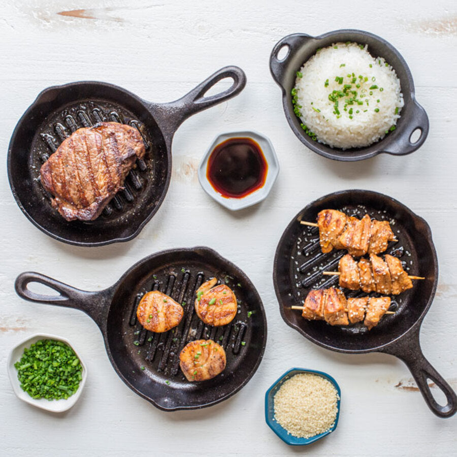 A variety of dishes made and served in pan on table including chicken, scallops, and steak all seared with lines from pan.
