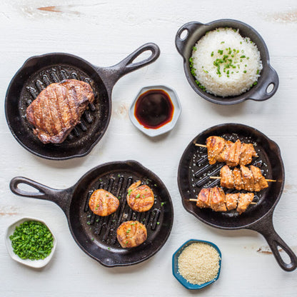 A variety of dishes made and served in pan on table including chicken, scallops, and steak all seared with lines from pan.