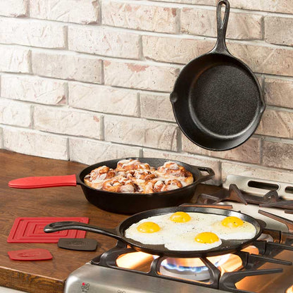 A set of seasoned cast iron skillets and a griddle with red silicone handles and accessories displayed on a kitchen counter.